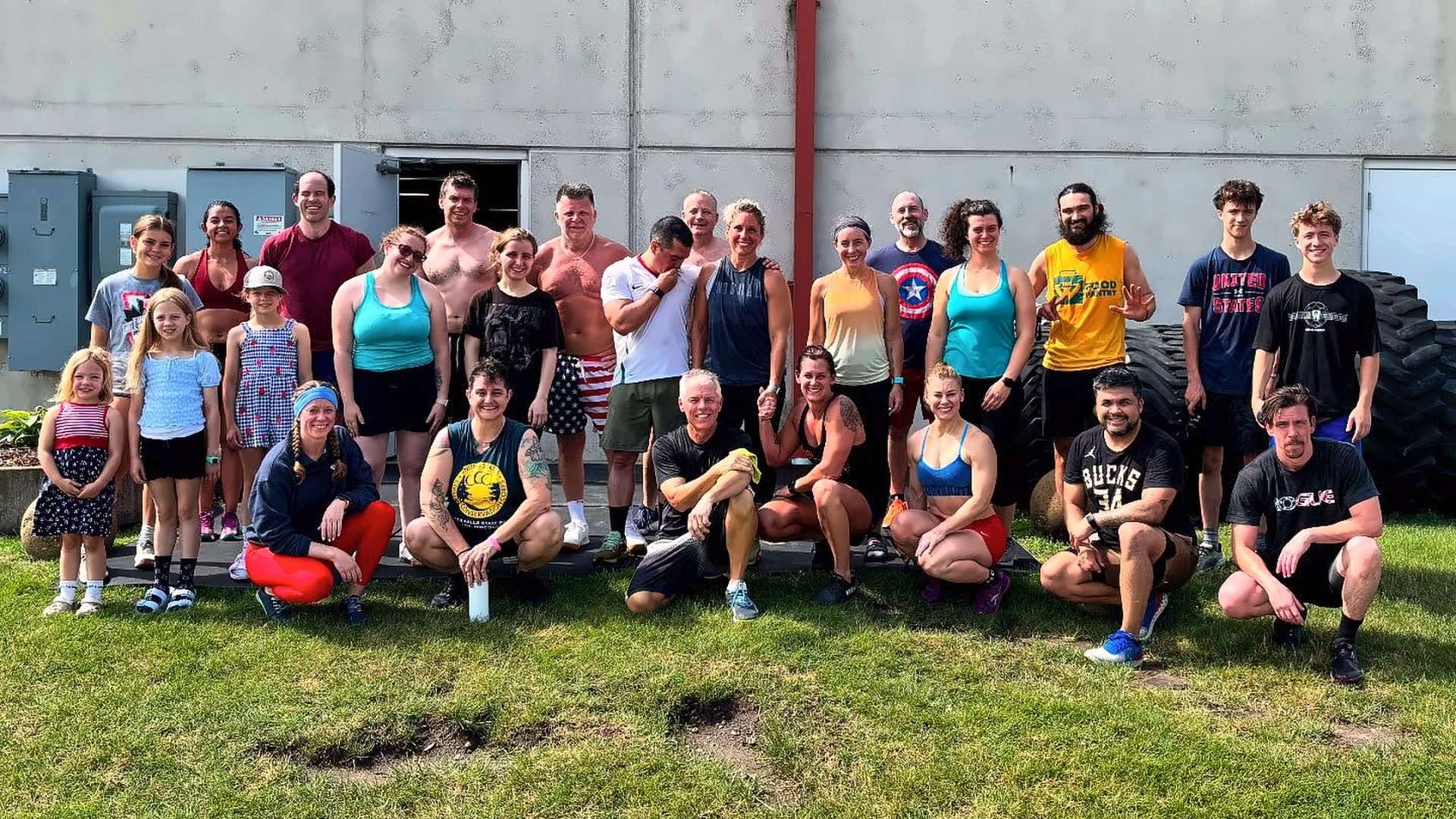A big MadCity community group, families and kids included, on the grass outside the gym